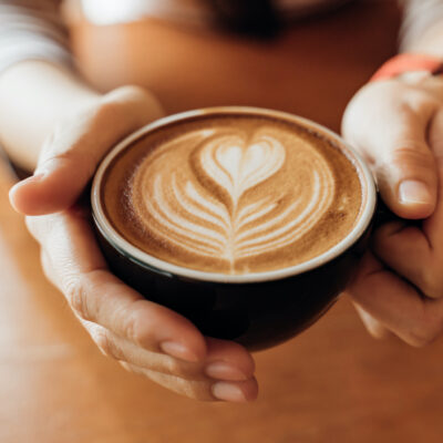 Zwei Hände halten eine Tasse Cappuccino mit einer herzförmigen Milchhaube