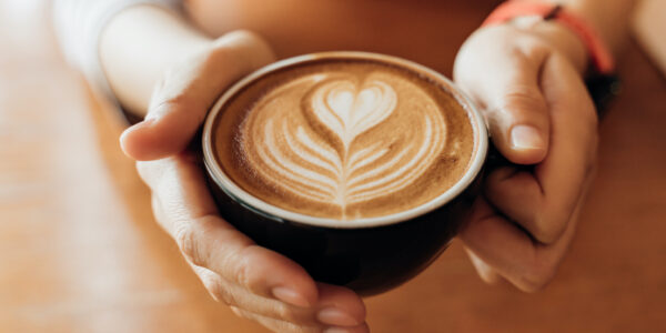 Zwei Hände halten eine Tasse Cappuccino mit einer herzförmigen Milchhaube